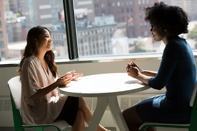 Two people talking at a table by a window