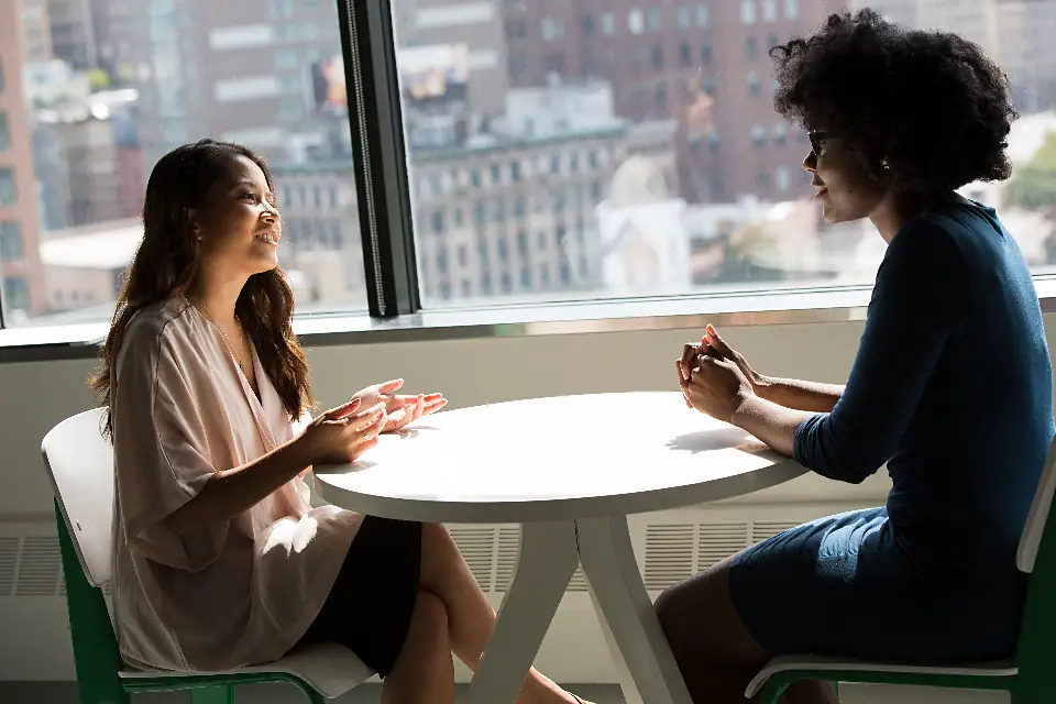 Two people talking at a table by a window